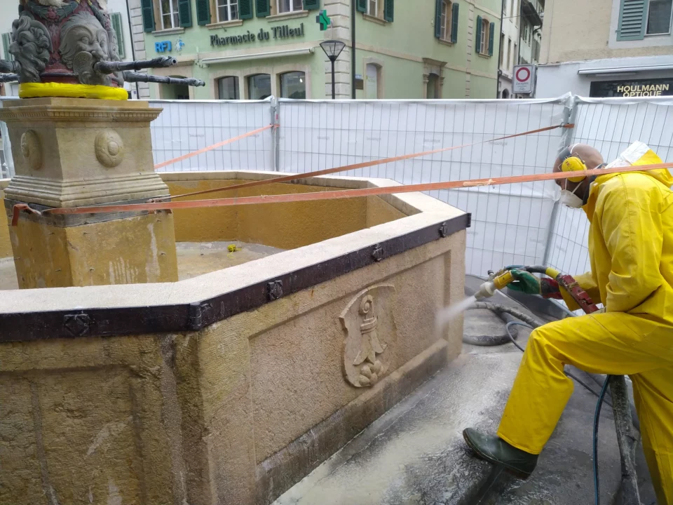 Opérateur Ma-Tek en tenue de protection nettoyant une fontaine historique en pierre par hydrogommage