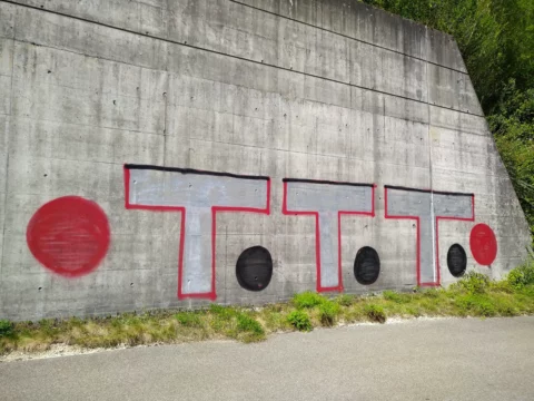 Betonstützmauer mit einem grossen Graffiti vor der Reinigung